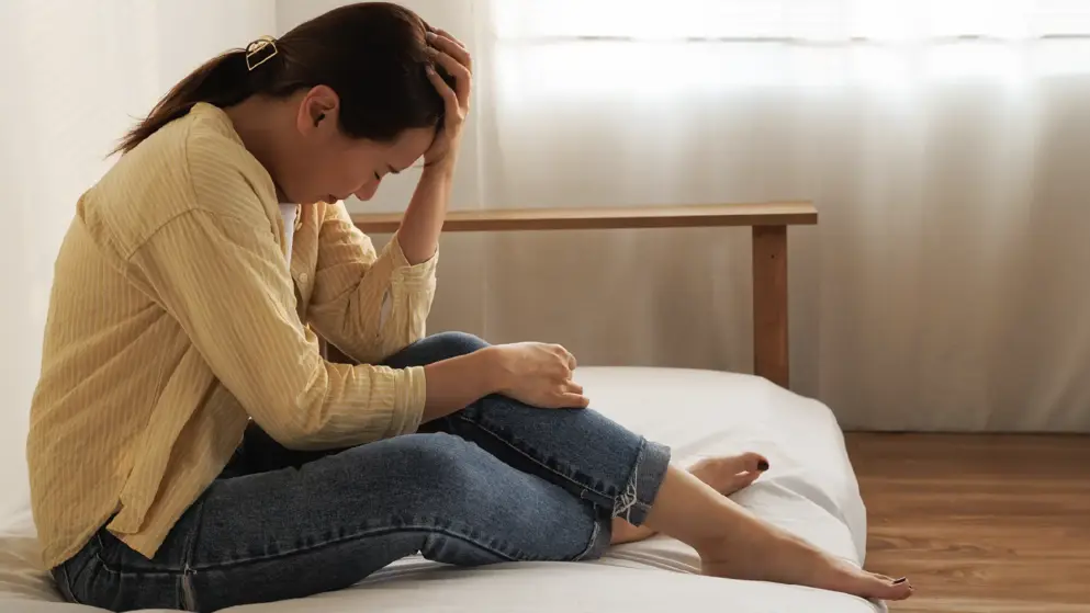 Woman sitting down on bed with head in hands