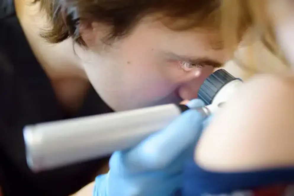 A dermatologist looks at a rash on the back of a girl using a dermatoscope.